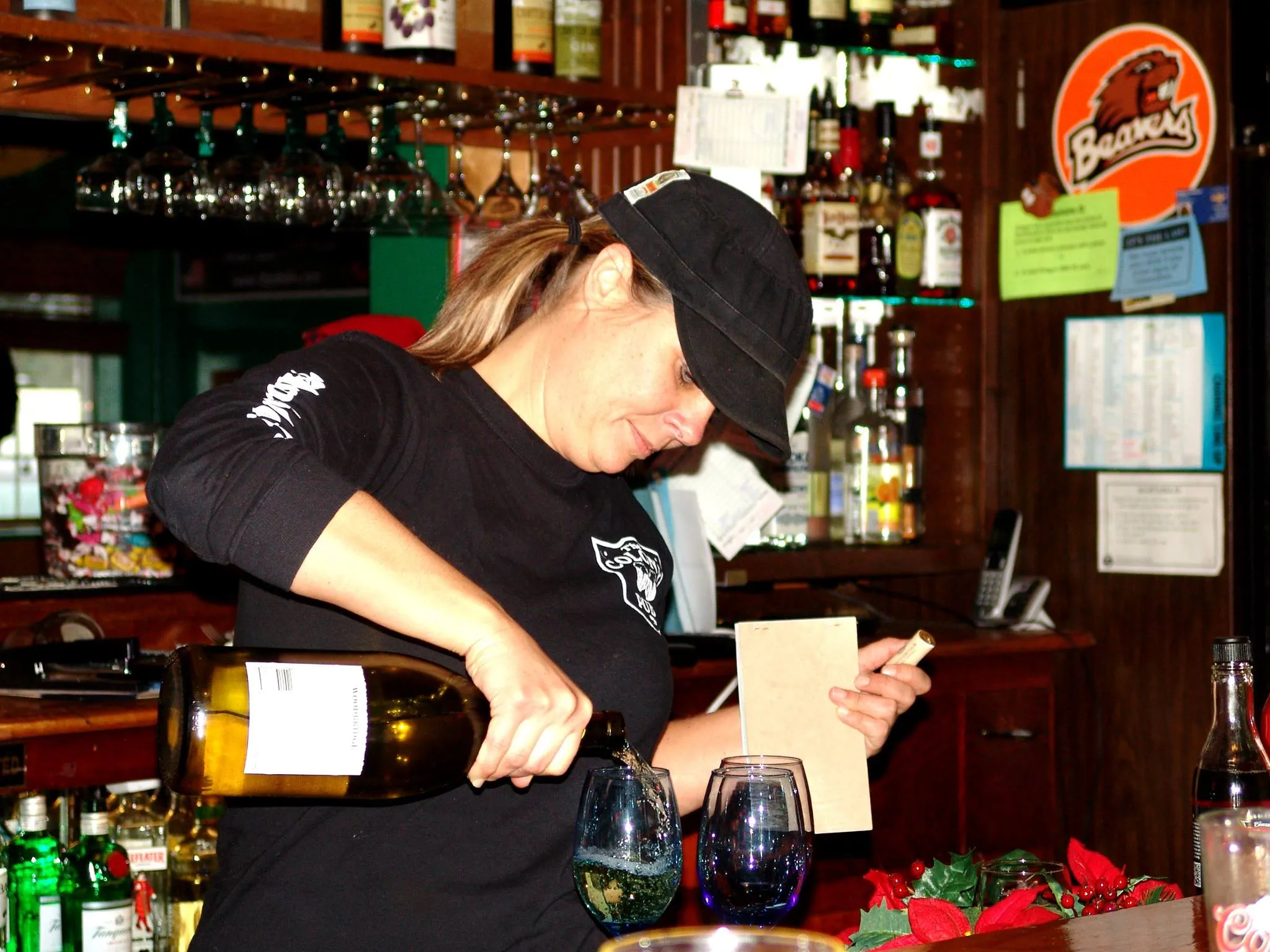 Bartender mid-pour over two glasses, the lineup of bottles glowing behind the bar.