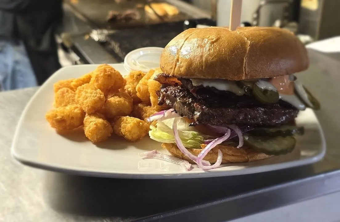 A double bacon cheeseburger on a toasted bun with a side of crispy tater tots.
