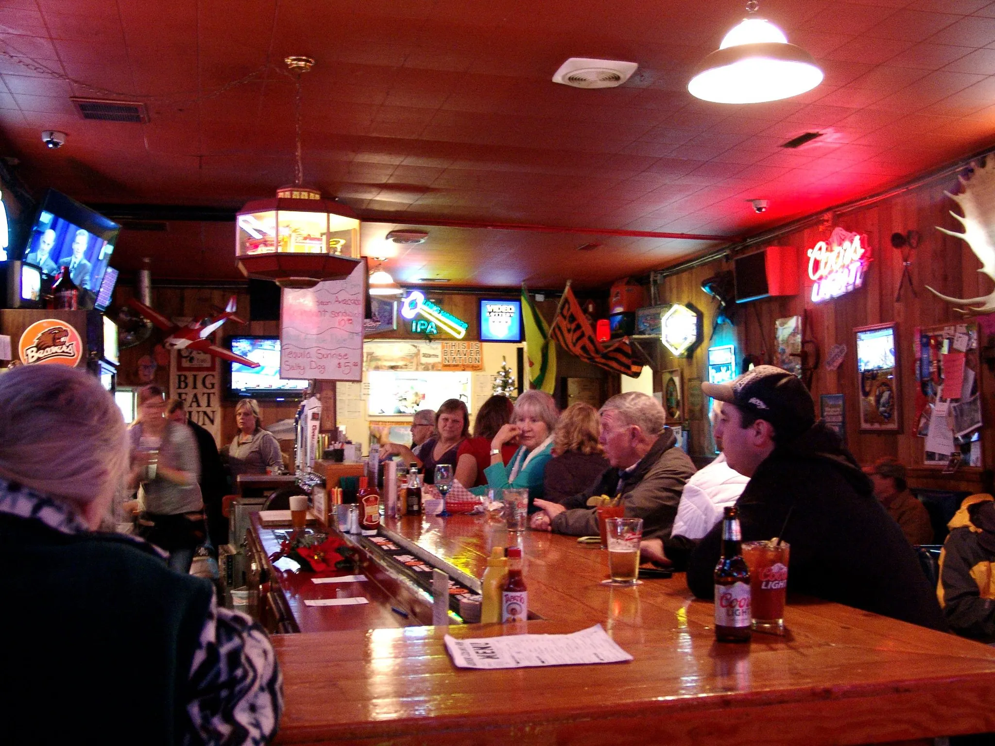 Red ceiling glowing over the bar, neon signs reflecting off the wood, bartender pouring drinks.