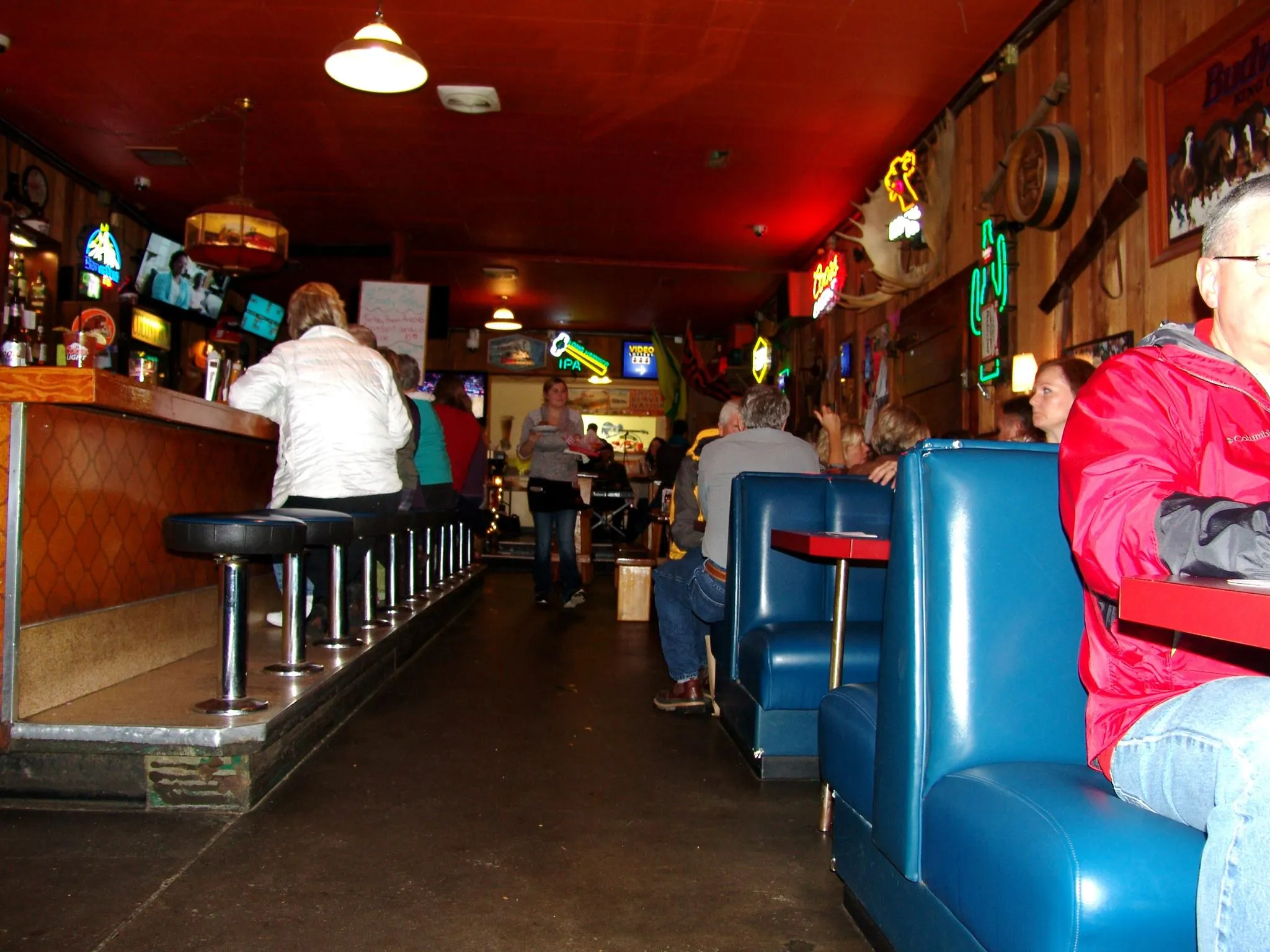Vintage blue booth along the side wall, red ceiling overhead, neon signs hanging above the bar.