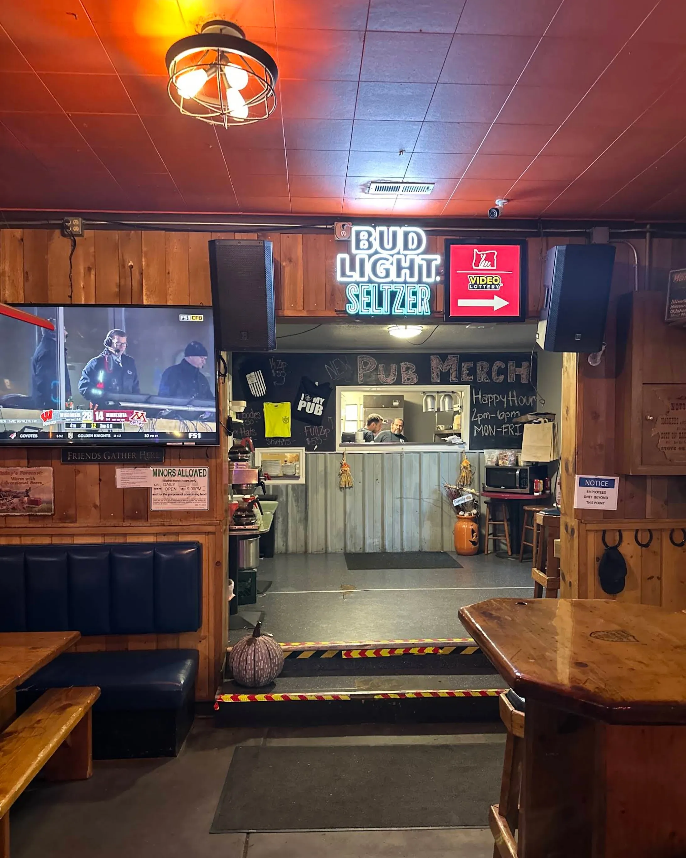 The pub merch counter glowing under a neon sign, framed by warm wood paneling and blue booths.
