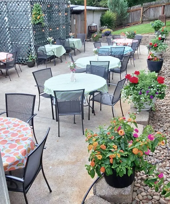 The flower-filled patio from above — round tables, string lights and overflowing baskets of summer blooms.